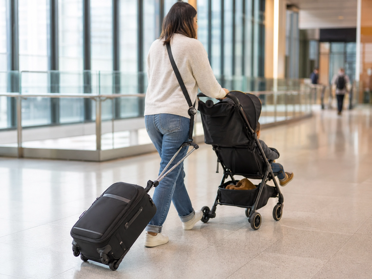 Traveler using a shoulder luggage strap to reduce arm and shoulder strain while moving through an airport.