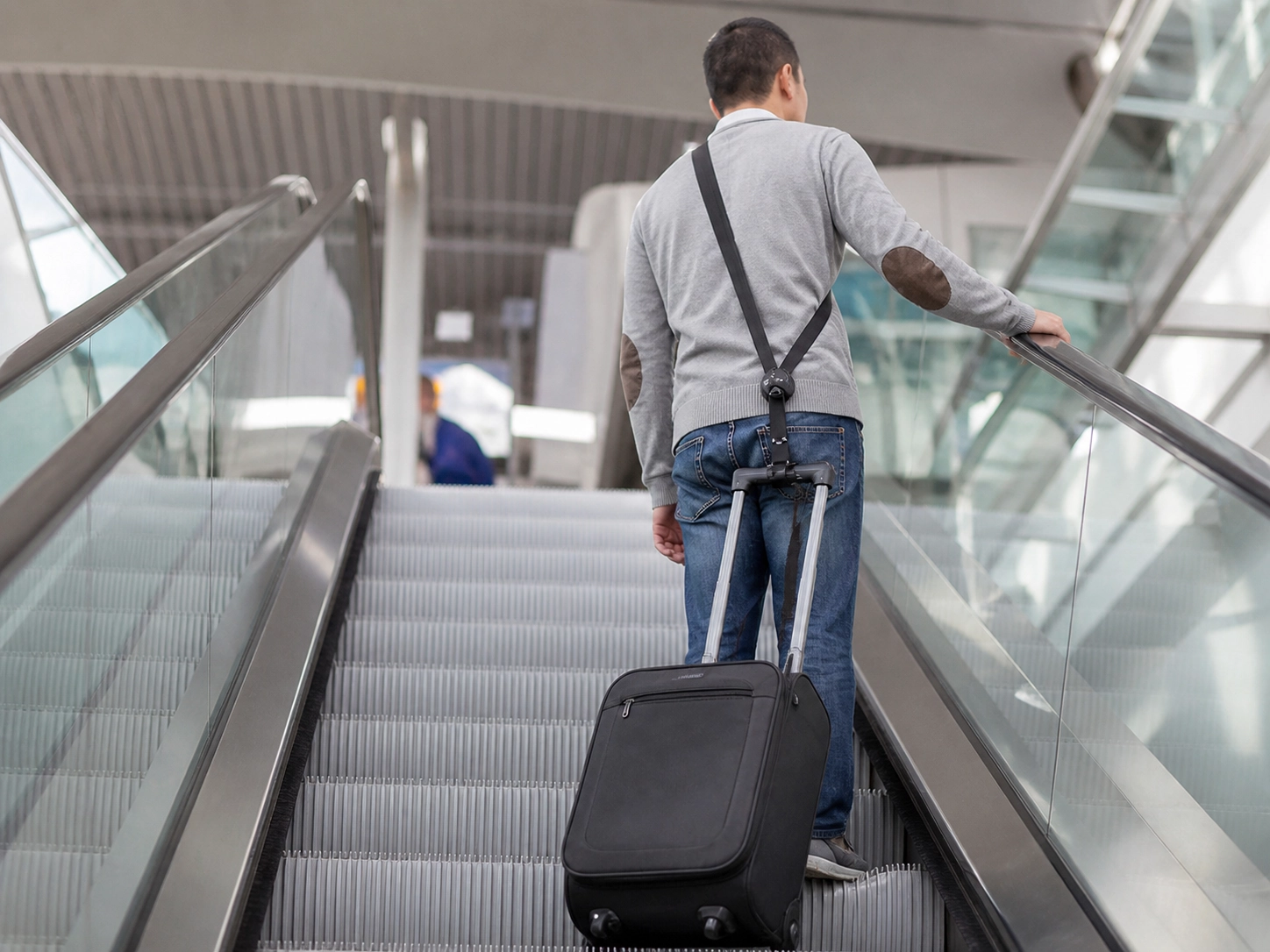 Traveler using a hands-free luggage strap on an escalator for added control and safety.