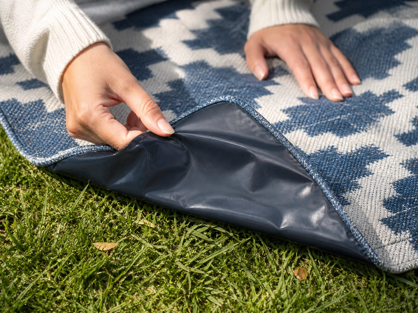 Close-up of a picnic blanket corner showing waterproof backing on grass.
