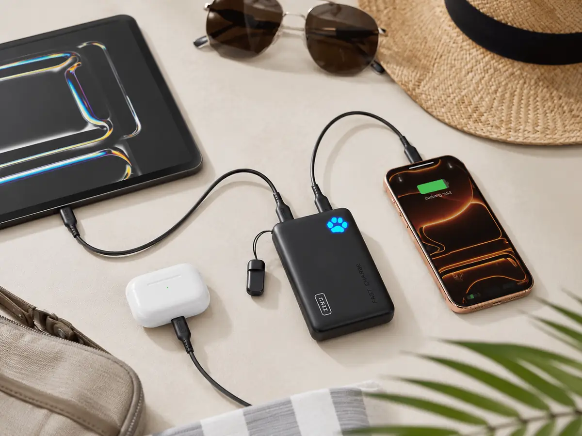Portable charger powering summer travel devices on a clean table with phone, tablet, and earbuds.