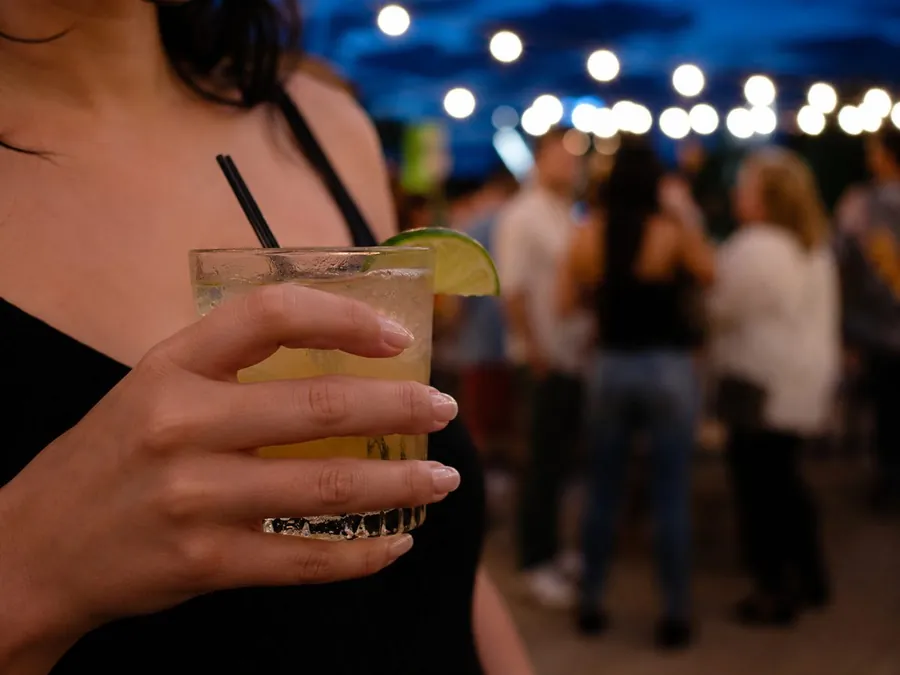 A person holding their own drink at a crowded summer night venue.