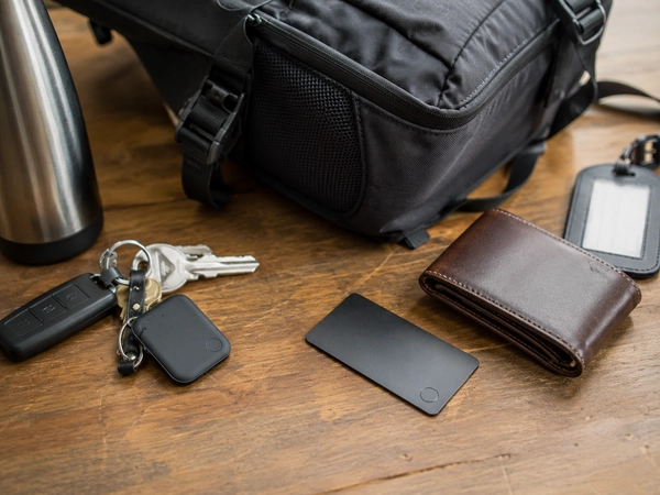 Smart tracking tags placed beside keys, a wallet, a backpack, and a luggage tag